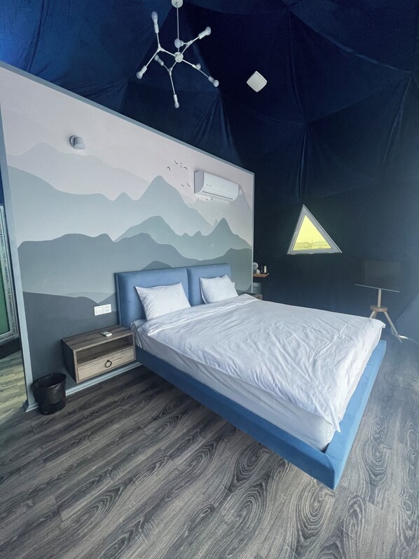 Un dormitorio con cama, mesita de noche, aire acondicionado de pared, lámpara en el techo y una ventana triangular.