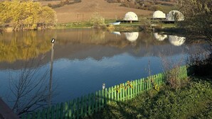 A serene lakeside view with two dome-shaped yurts, a wooden fence, and a clear blue sky. - Chadir yurd glamp (Ismailli)