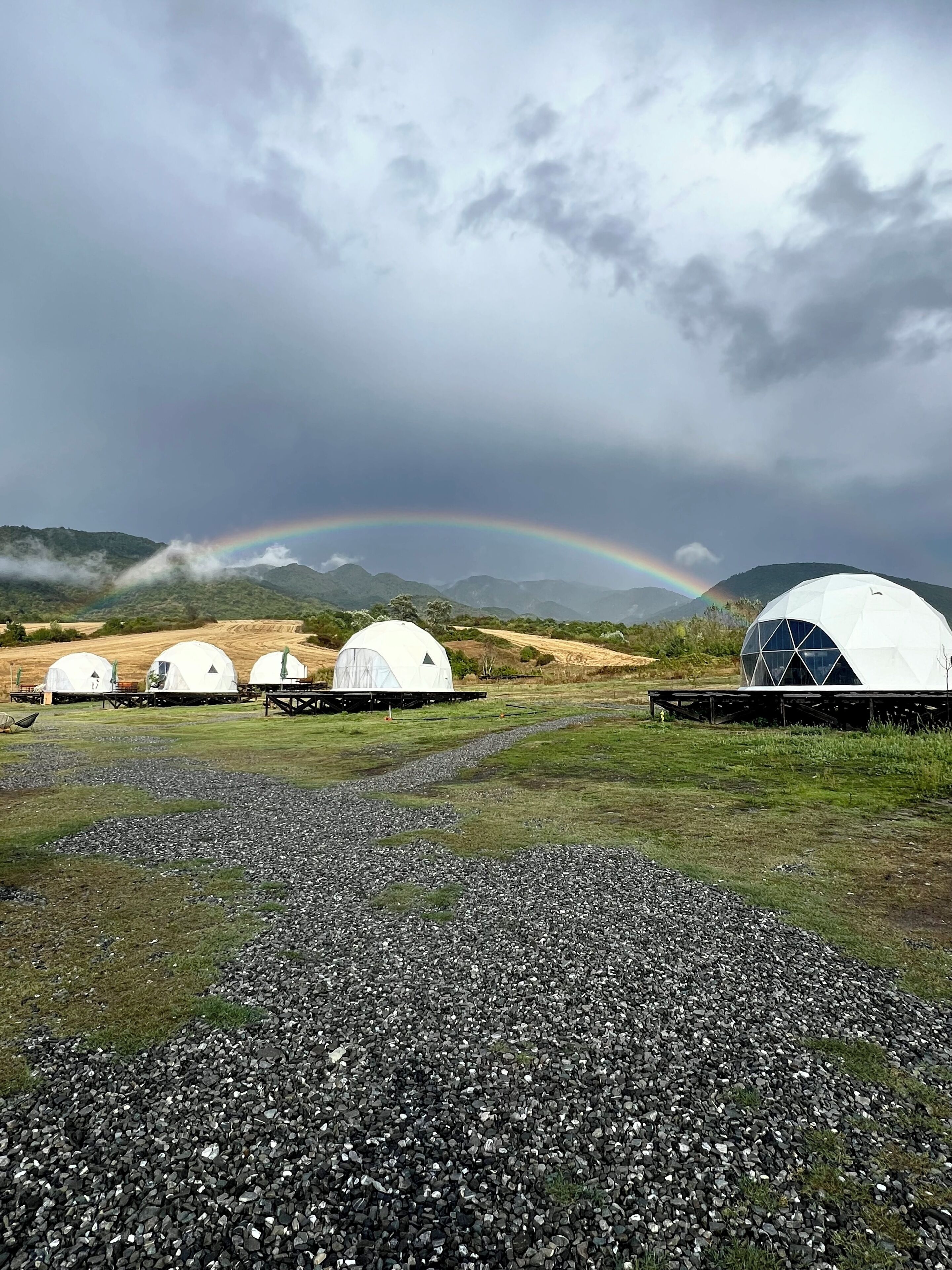 A series of dome-shaped structures in a natural setting with a rainbow in the background.