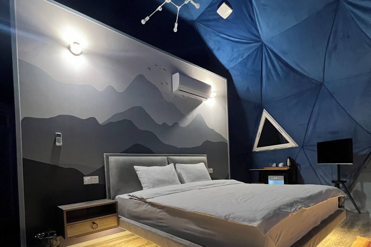 A modern bedroom with a bed, bedside tables, a wall-mounted air conditioner, and a geometric-patterned wall.