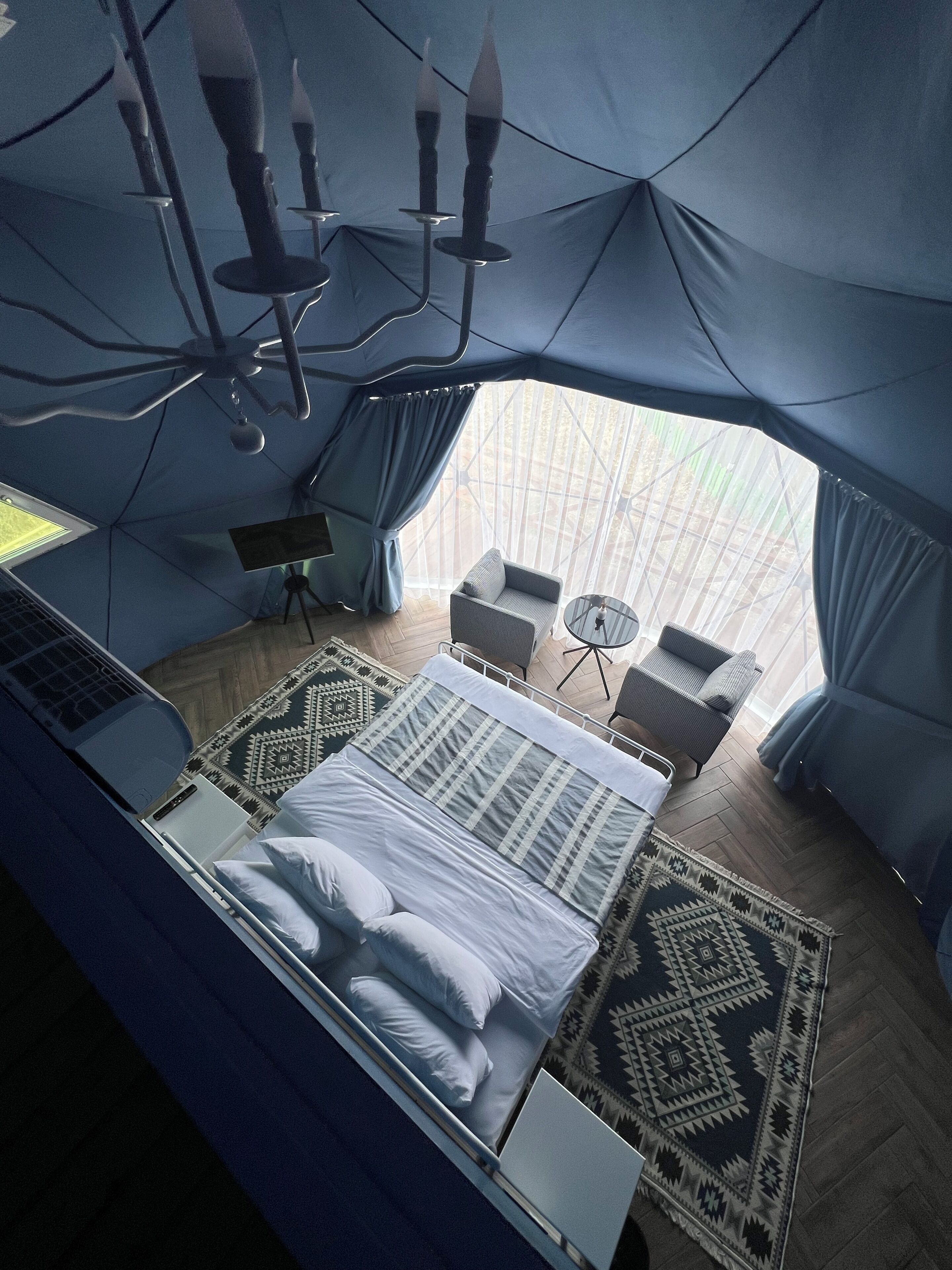 A tent-style room with a bed, a desk with a laptop, a chair, and a small table.