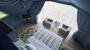 A tent-style room with a bed, a desk with a laptop, a chair, and a small table.