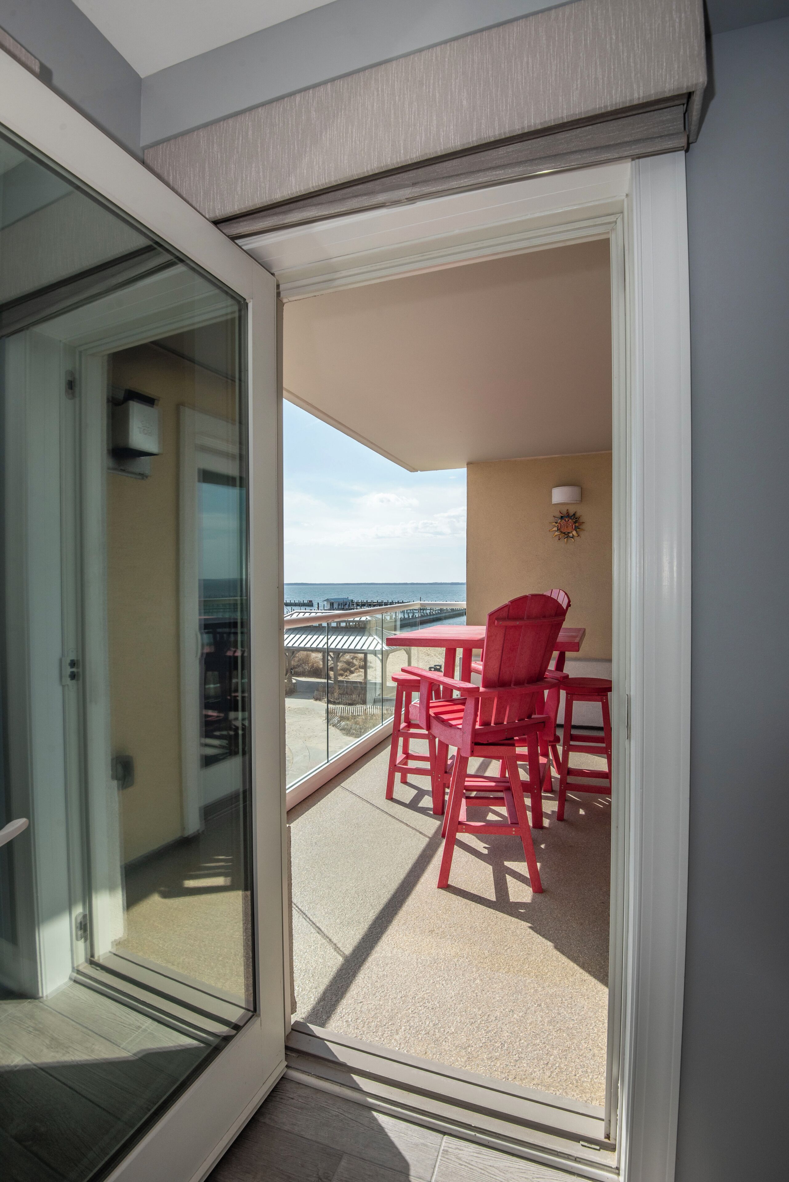 Un balcone con tavolo e sedie, una porta in vetro e vista sulla spiaggia.