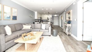 Un soggiorno moderno con un divano grigio, un tavolino in legno e una cucina sullo sfondo.