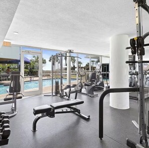 Ein Fitnessstudio mit Trainingsgeräten, einer Bank und einem Pool im Hintergrund.