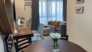 Ein modernes Wohnzimmer mit Esstisch, Sofa, Sessel und einer dekorativen Vase mit weißen Blumen.