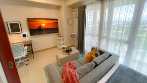 Ein modernes Wohnzimmer mit einer Couch, einem Schreibtisch, einem Sessel, einem Gemälde und Blick ins Freie.