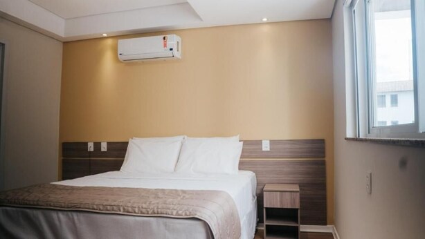 A hotel room with a bed, bedside table, and an air conditioning unit. - HOTEL GOLDEN INN (Conselheiro Lafaiete)