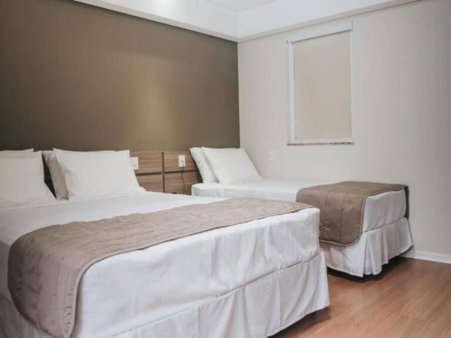 A hotel room with two beds, a bedside table, a window, and a wooden floor.