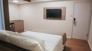 Une chambre avec un lit, un téléviseur fixé au mur, une porte et un coin cuisine.