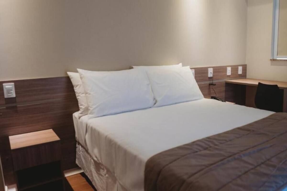 A hotel room with a bed, bedside tables, a desk, and a chair.