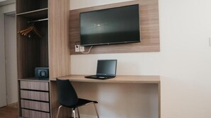 A room with a desk, a chair, a TV mounted on the wall, a wardrobe, and a small safe. - HOTEL GOLDEN INN (Conselheiro Lafaiete)