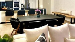 Une cuisine moderne avec un coin repas, comprenant un îlot central, un éclairage suspendu et un canapé agrémenté d’un coussin à motifs.