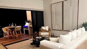 Un salon moderne avec un canapé, un coin repas avec des chaises, un ventilateur de plafond et des œuvres d’art abstraites accrochées au mur.