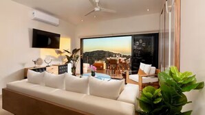 A modern living room with a sofa, a dining area, and a large window with a view. - Oceanfront Luxury Boutique Villa-Pool, Spas, Fitness, Yoga-Casa Luxe at Cerritos (Los Cerritos)