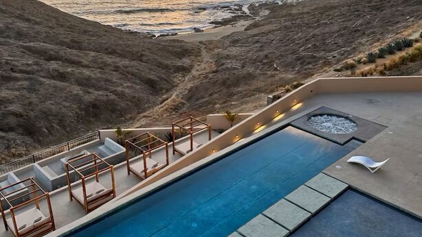 Une piscine avec des chaises longues et une vue sur l’océan au coucher du soleil.