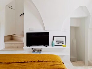 Ein Schlafzimmer mit Fernseher, einem gerahmten Foto, einem Buch und einem Bett mit gelber Bettdecke.