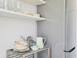 A kitchen with a stainless steel refrigerator, a glass shelf with dishes, and a metal table with bowls and utensils. - A Casa di Rò by Wonderful Italy (Ostuni)