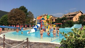 Ein Poolbereich mit Wasserrutsche und Spielgeräten, umgeben von Liegestühlen und Sonnenschirmen.