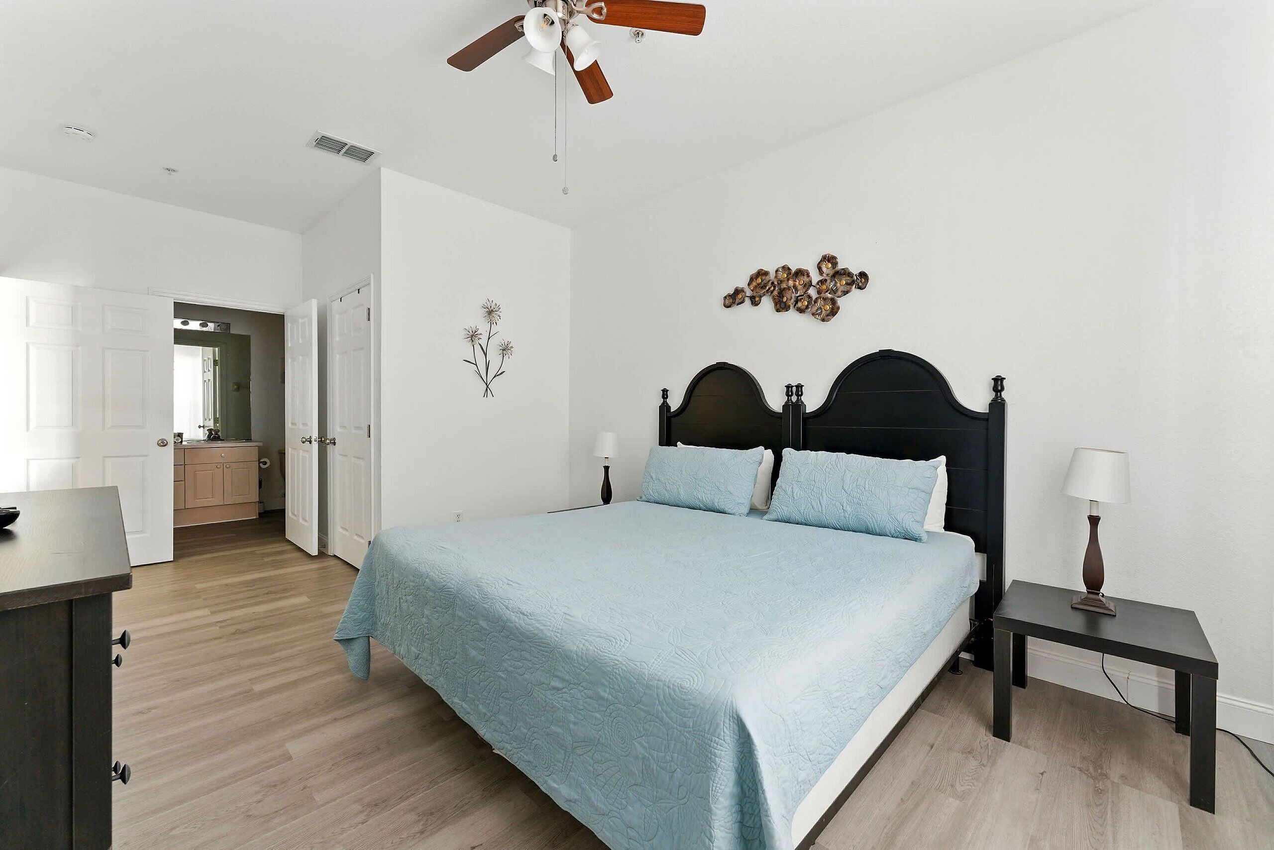 A bedroom with a bed, bedside tables, a ceiling fan, and a view into the adjacent room.