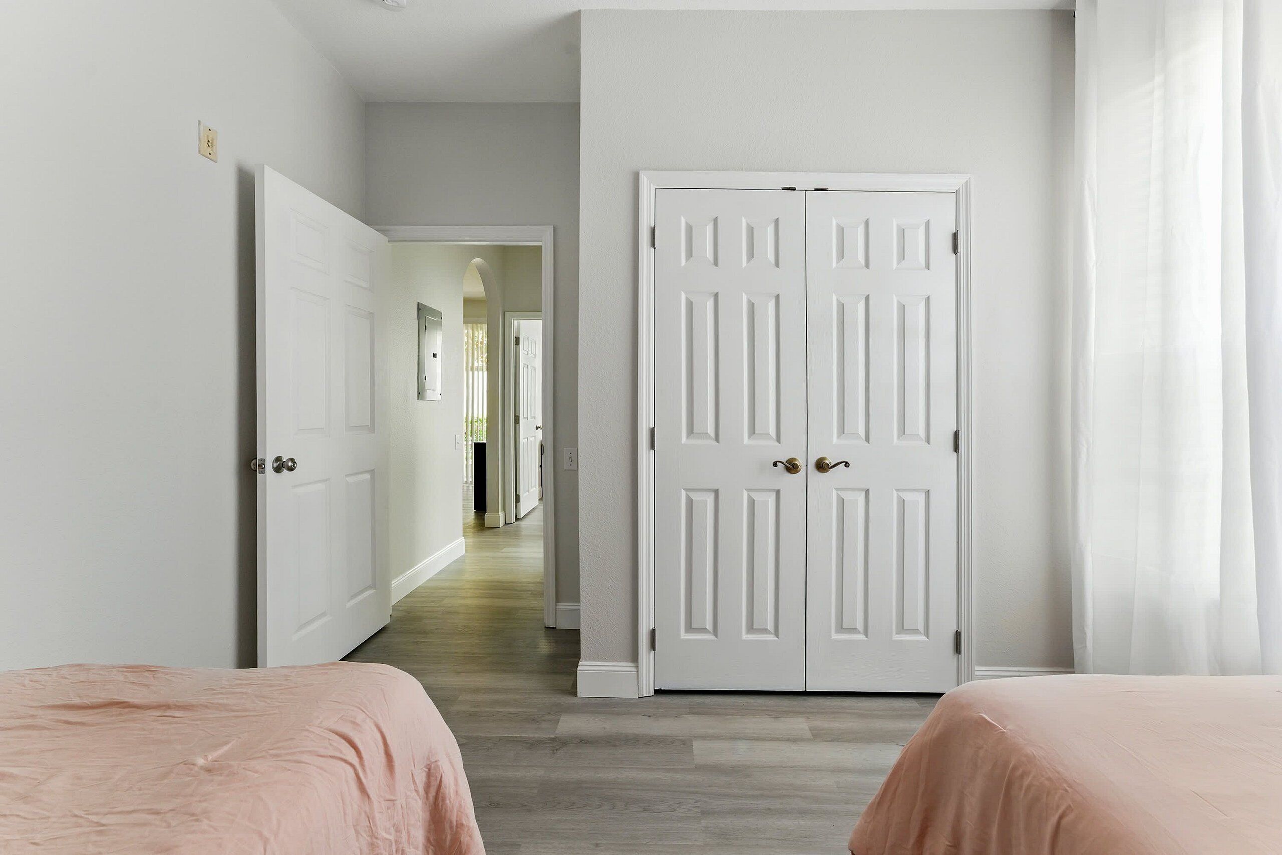 Un pasillo que conduce a una puerta blanca, una cama con colcha rosa y otra cama con una colcha similar.