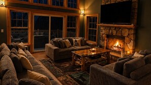 A cozy living room with a stone fireplace, a ceiling fan, and a large window with multiple panes. - Moonlight Mountain Lodge at Camelback Mountain! (Tannersville)