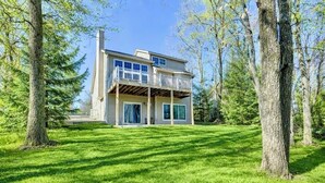 A two-story house with a covered porch, surrounded by trees and a well-maintained lawn. - Moonlight Mountain Lodge at Camelback Mountain! (Tannersville)