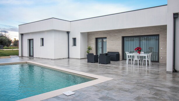 Ein moderner Außenpoolbereich mit einem rechteckigen Pool, einem Esstisch mit Stühlen und einem kleinen Garten mit einem Topfpflanzen.