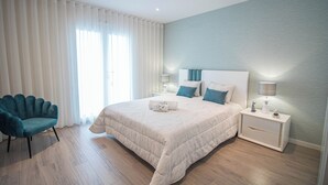 Ein modernes Schlafzimmer mit einem großen Bett, Nachttischen, einem Sessel und Blick ins Freie.