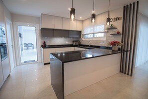 Eine moderne Küche mit einer großen Kochinsel, Pendelleuchten und Blick zum Essbereich.