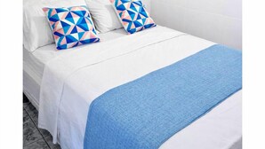 A bed with white bedding, two patterned pillows, a blue throw blanket, and a wall with three circular wall art pieces. - VEREDA 7 SUITES (São Sebastião)