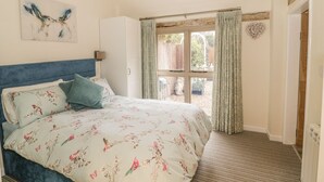 A bedroom with a bed, a window with curtains, a wooden ceiling beam, and a wall-mounted artwork. - Megs Cottage (Stratford-upon-Avon)