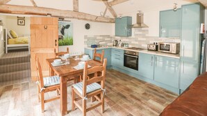 A rustic kitchen with wooden beams, a dining table with chairs, and light blue cabinets. - Megs Cottage (Stratford-upon-Avon)