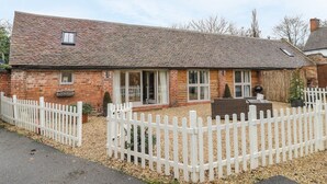 A brick house with a white picket fence, a small garden, and a clear sky. - Megs Cottage (Stratford-upon-Avon)
