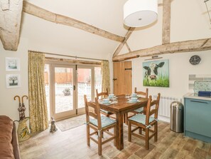 A dining area with a wooden table and chairs, a clock on the wall, and a view through a glass door. - Megs Cottage (Stratford-upon-Avon)