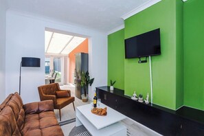 A modern living room with a sofa, armchair, and coffee table, a flat-screen TV mounted on a green wall, and a view through a glass door to an outdoor area. - Chesterton Haven - 3BR Modern & Spacious Living (Chesterton)