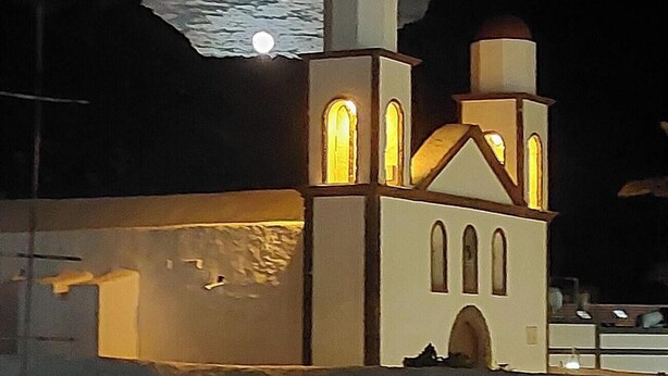 Une église à deux tours, dotée de fenêtres en arc de cercle, avec une lune en arrière-plan.