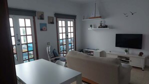 Une chambre avec un lit, une télévision, un bureau et une chaise. Il y a des fenêtres donnant sur l’extérieur.