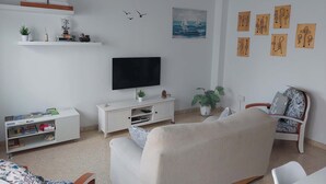 Un salon avec un téléviseur, des meubles blancs, une bibliothèque et des œuvres d’art murales.