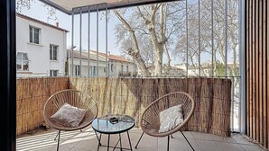 En balkon med to fletstole, et lille rundt bord og udsigt til bygninger og træer.