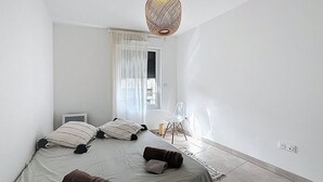 Et soveværelse med seng, puder, stol, lampe og et vindue med gardiner.