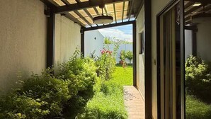 A covered outdoor corridor with a wooden floor, leading to a glass door.