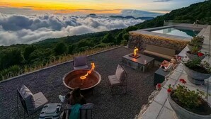 A rooftop terrace with a fire pit, seating, and a view of clouds and mountains.