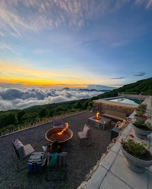 Una terraza en la azotea con una chimenea, asientos y vistas a las nubes y montañas.