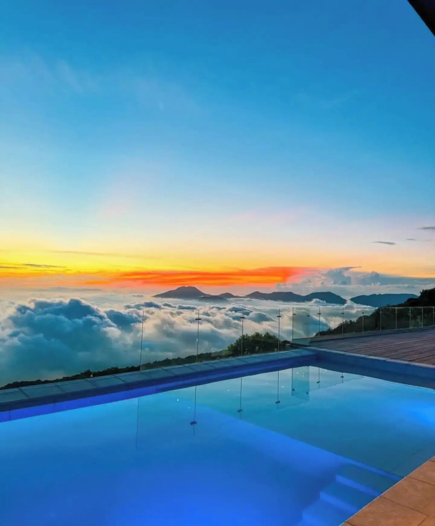 Cielo despejado con un atardecer, una piscina y vistas a nubes y montañas.