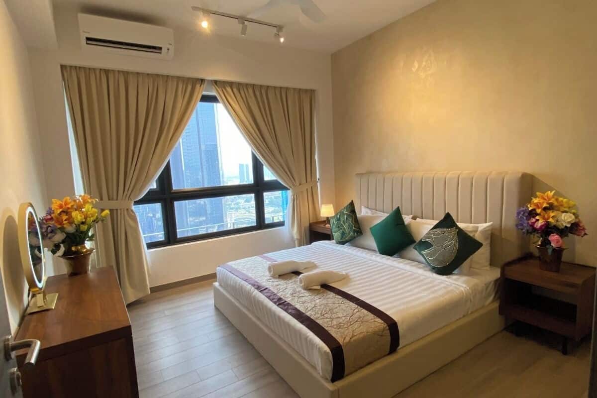 Habitación de hotel con cama, tocador con espejo, ventana con cortinas, ventilador de techo y vista de la ciudad.