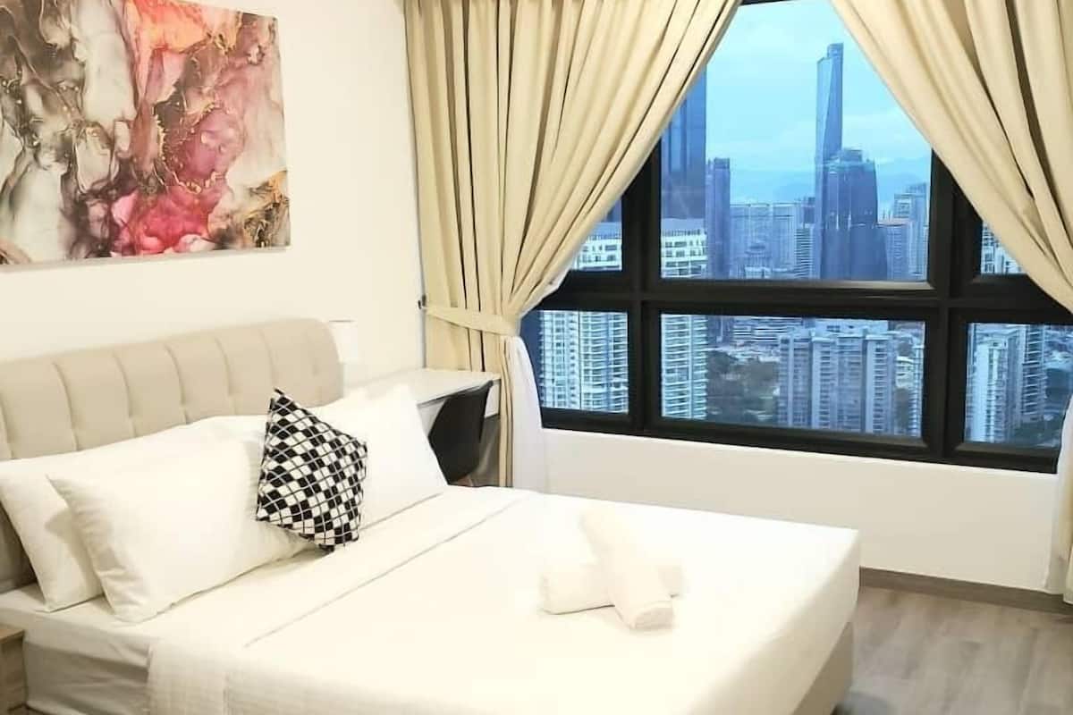 Habitación de hotel con cama, ventilador de techo, equipo de aire acondicionado, ventana con cortinas y vista panorámica de la ciudad.