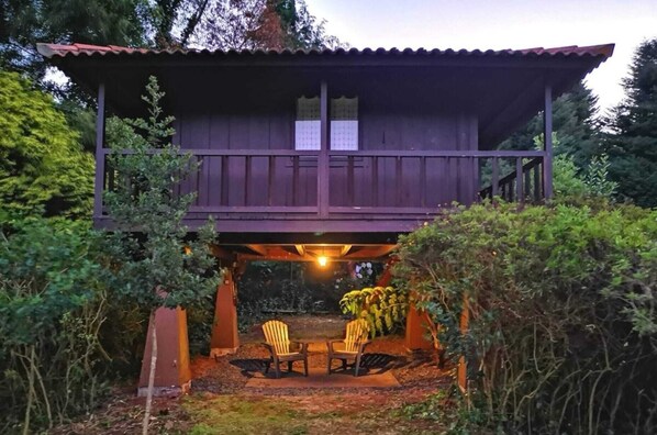 A wooden cabin with a balcony, a table with chairs, and a covered outdoor seating area.