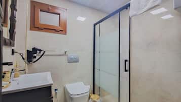 A bathroom with a toilet, a sink, a mirror, a towel, and a shower with a glass door.