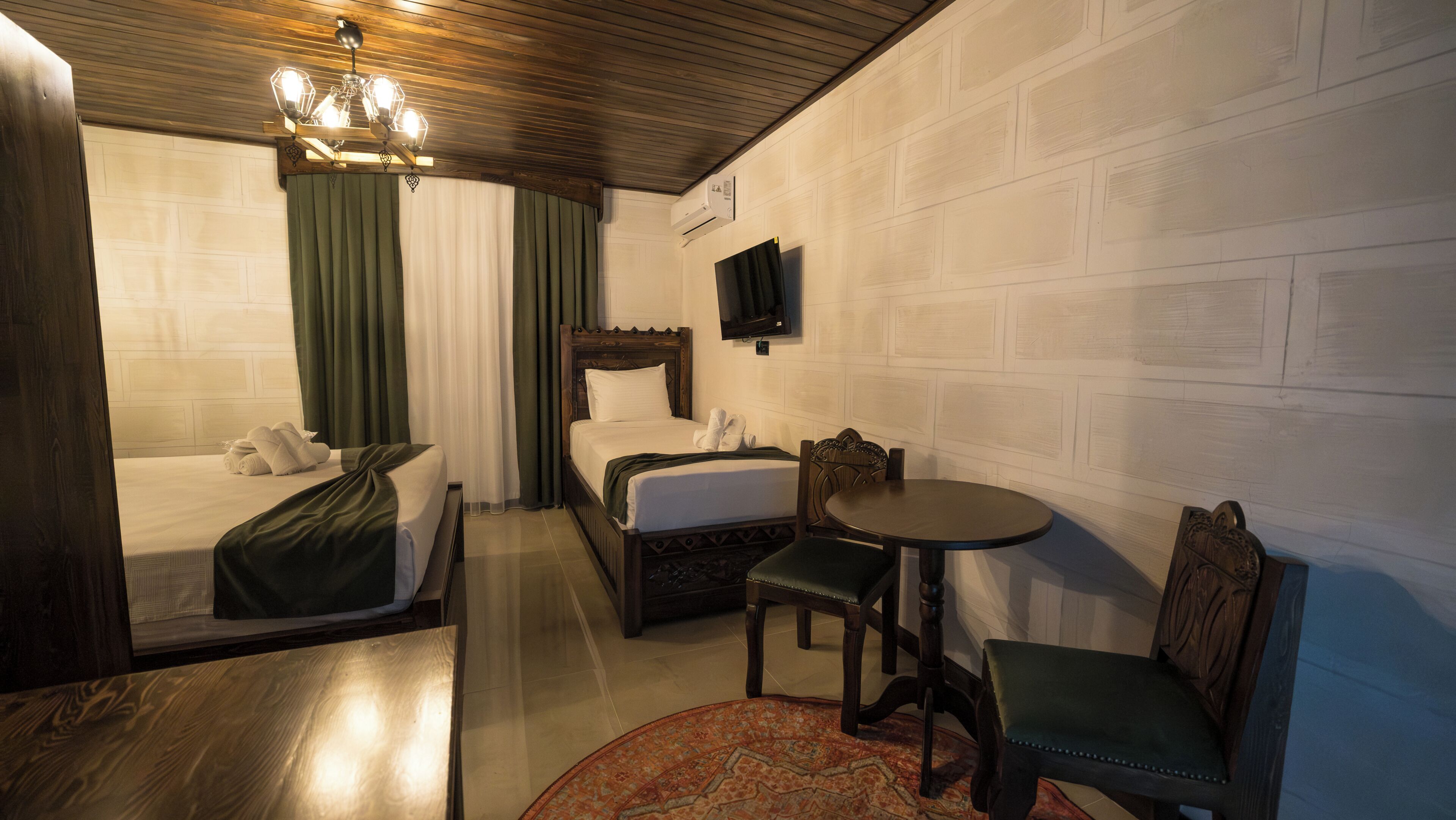 A hotel room with a bed, a desk, a chair, a television, and a chandelier.
